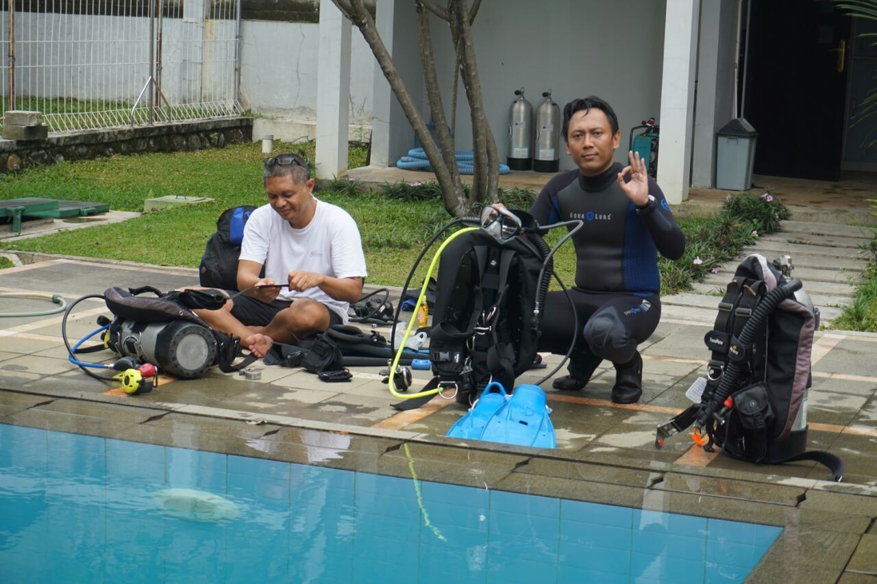 Nakula instructor giving the OK sign beside dive gear poolside