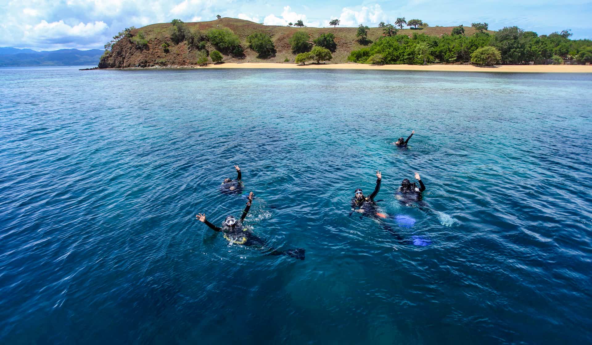 Nakula divers waving from the surface near an island beach